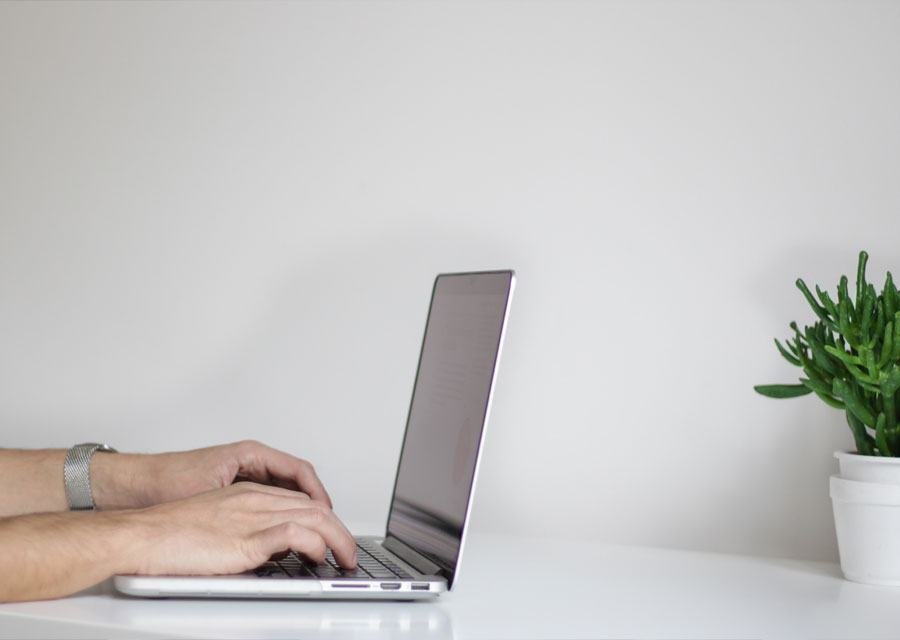 Hands typing on a laptop at a clean white desk